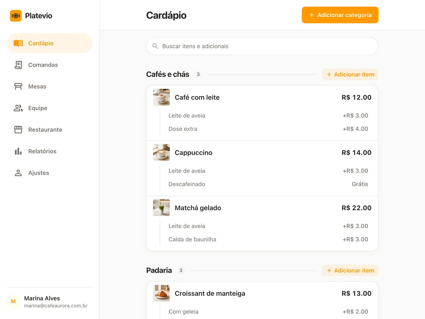A página Cardápio do Platevio em um tablet: a categoria Cafés e chás com cada item e o seu preço, embaixo de cada um os seus adicionais — leite de aveia, dose extra, um descafeinado grátis — e no alto o campo Buscar itens e adicionais